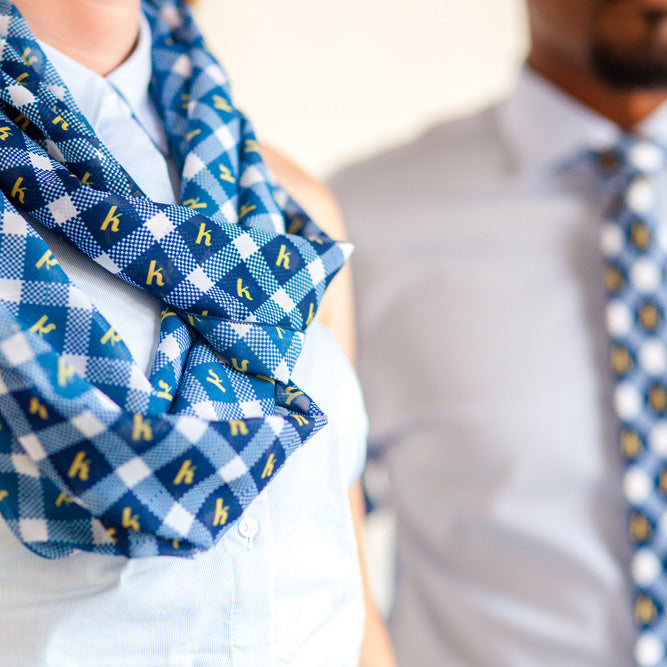 Person wearing a blue checkered custom scarf with yellow letters, blurred background