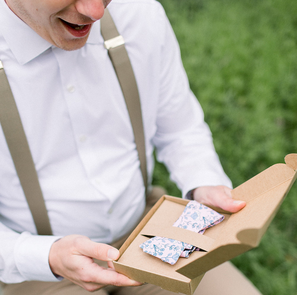man wearing suspenders opening bow tie box and smiling
