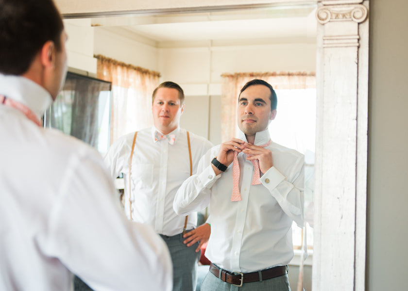 Groomsmen tying custom wedding bow tie in front of the mirror