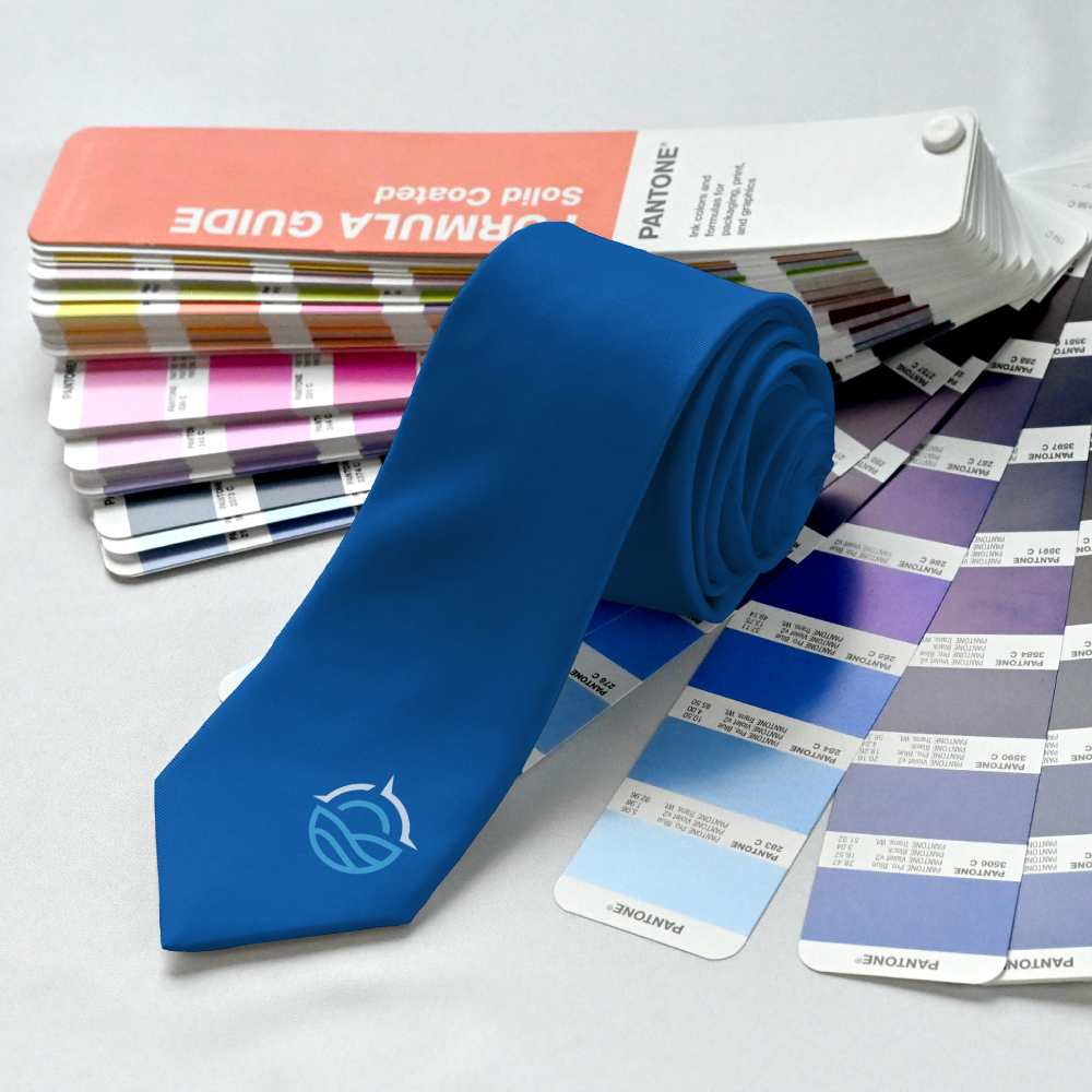 Rolled blue necktie placed near a matching blue Pantone color book swatch