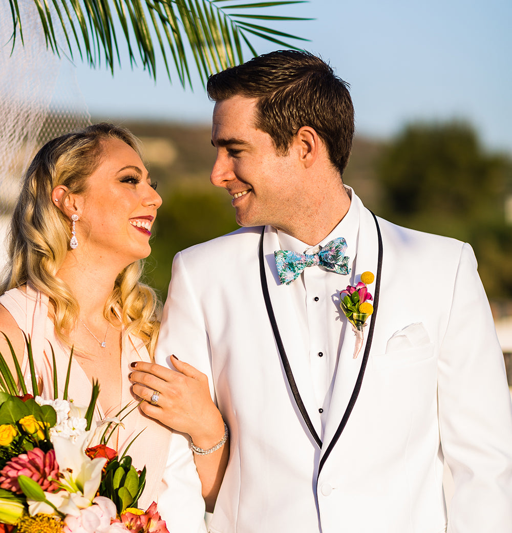 bride and groom wearing white with palm tree and tropical flowers