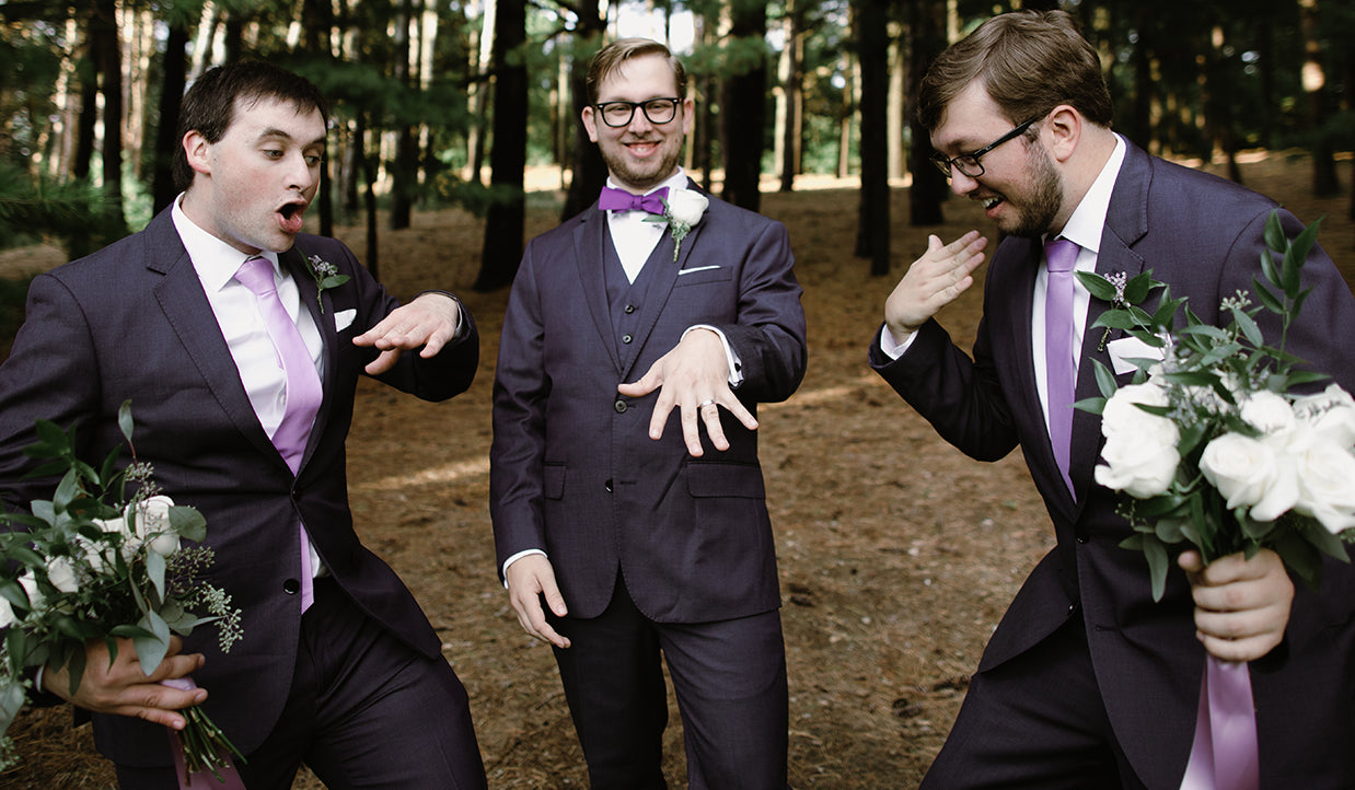 Groom and groomsmen goofing around in their wedding attire with purple ties and bow ties