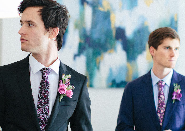 Men wearing custom floral wedding ties facing opposite direction with art on wall behind them