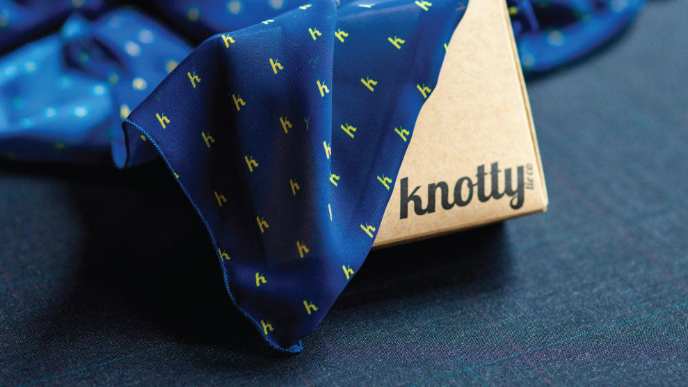 Blue patterned scarf with 'knotty' branding on a dark surface