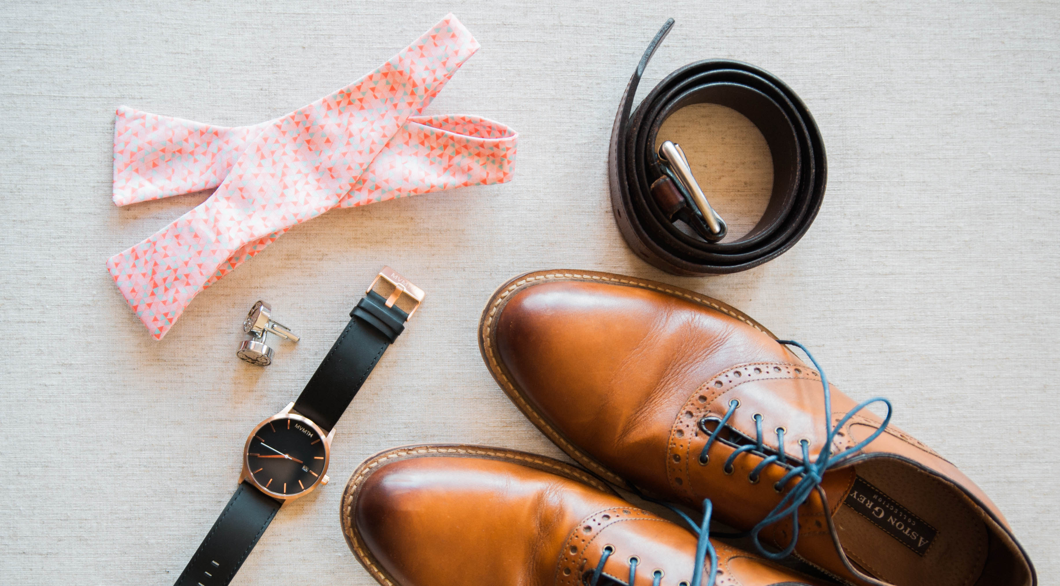 untied custom designed bow tie with belt and watch and shoes on table