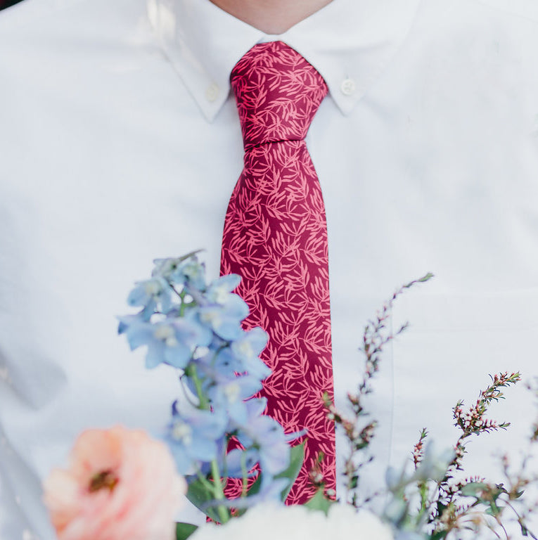 man wearing a red floral tie with flowers in the foreground of the image