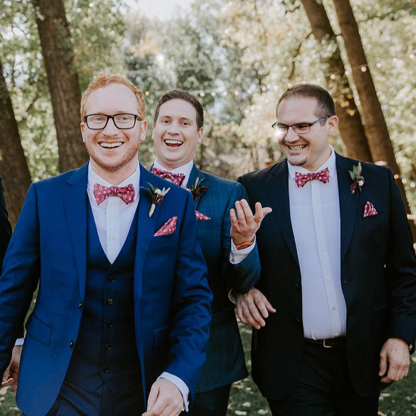 three men wearing blue suits and red bow ties at a wedding