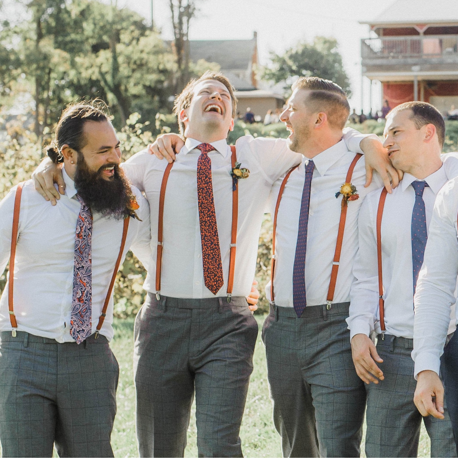 four groomsmen wearing neckties and suspenders having fun during a wedding