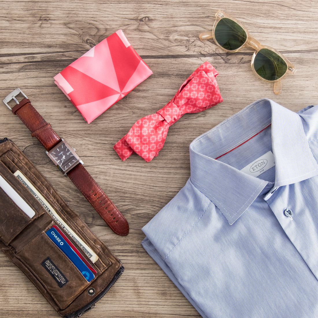top down photo of custom bow tie, folded pocket square, shirt, watch and sunglasses