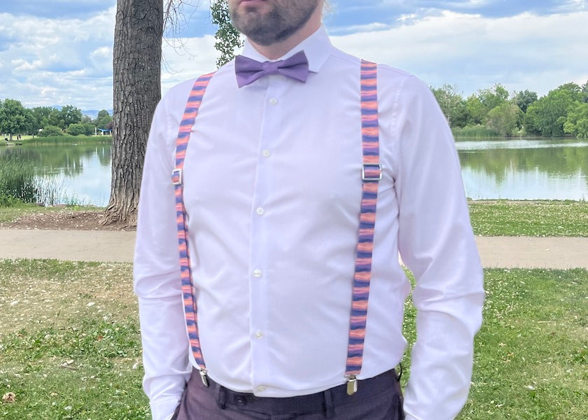 Man wearing matching bow tie and suspenders standing in park at wedding