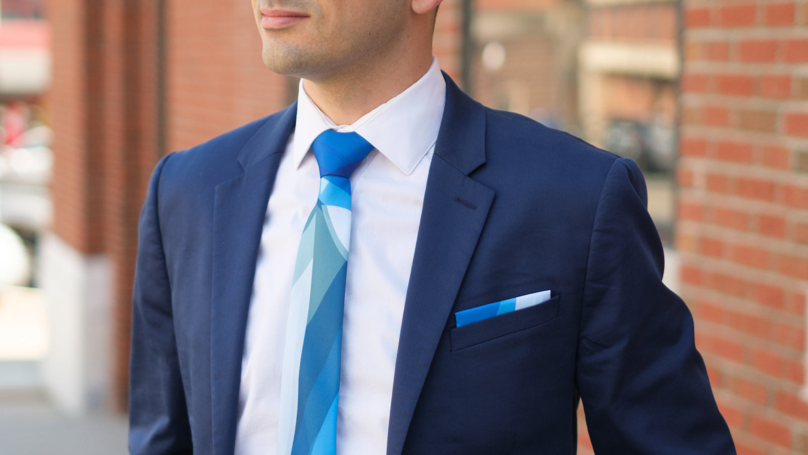 Man wearing a navy suit with a custom tie and pocket square against a brick wall.