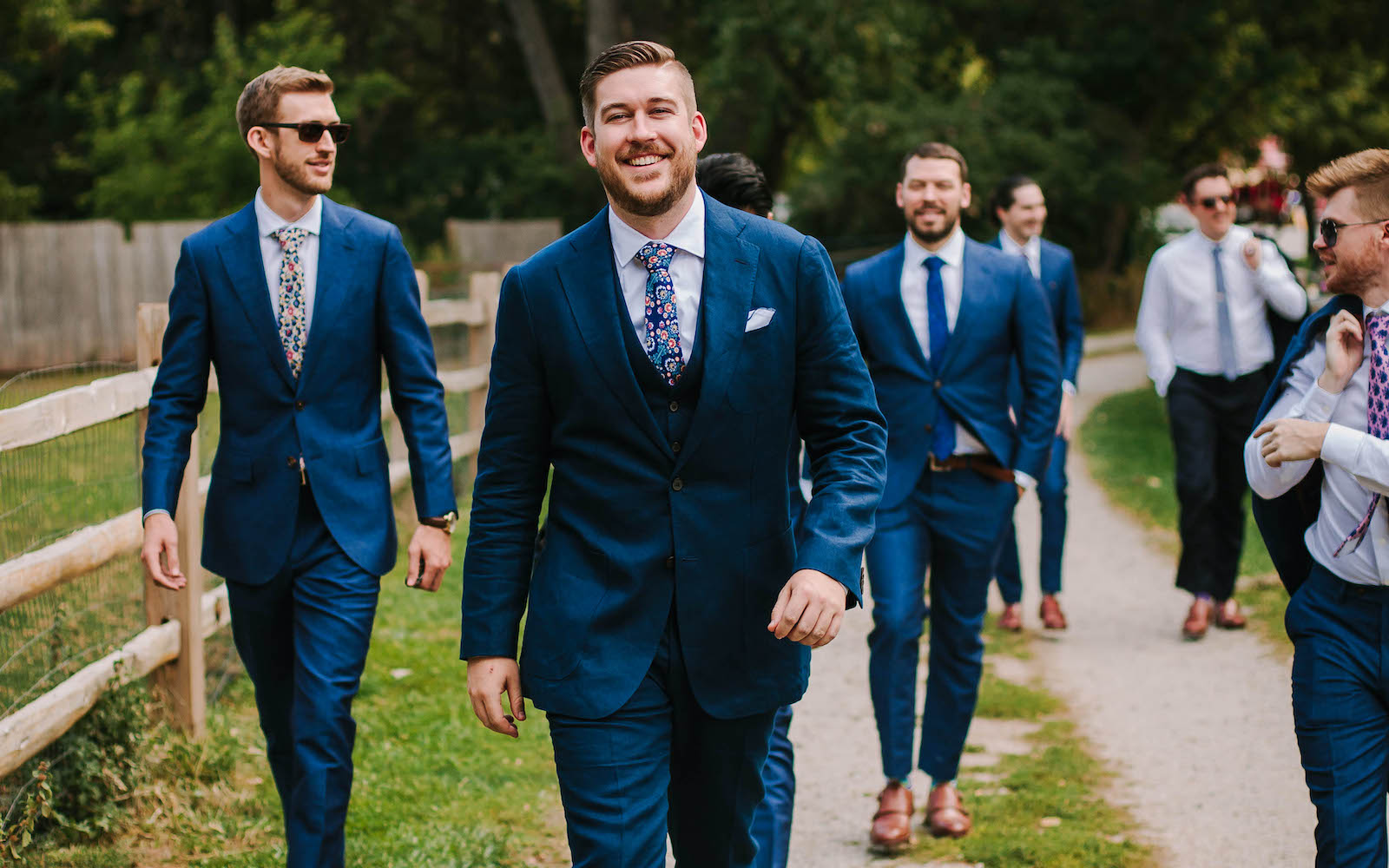 Groom and groomsmen in custom ties and blue suits walking.