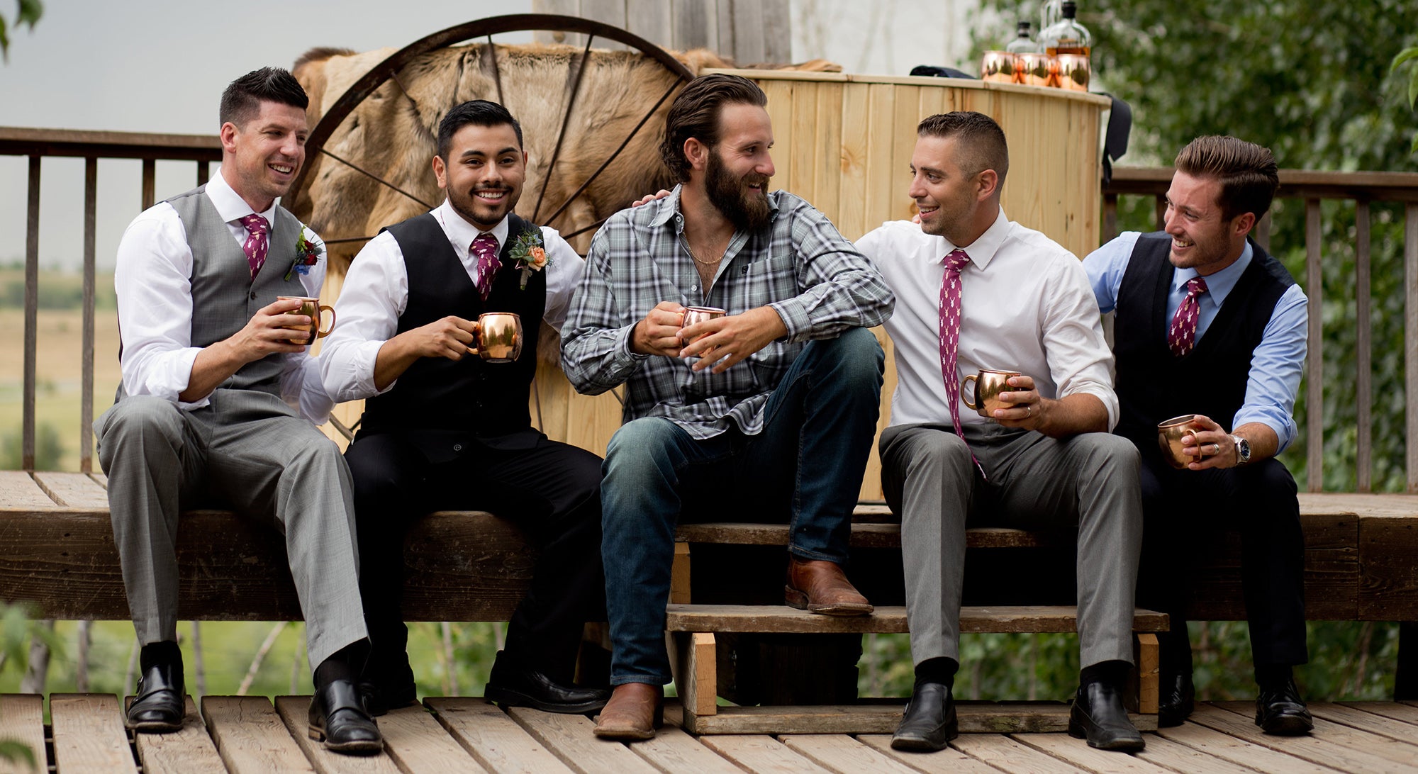 Five men sitting on a deck holding copper mugs wearing maroon ties with deer on them