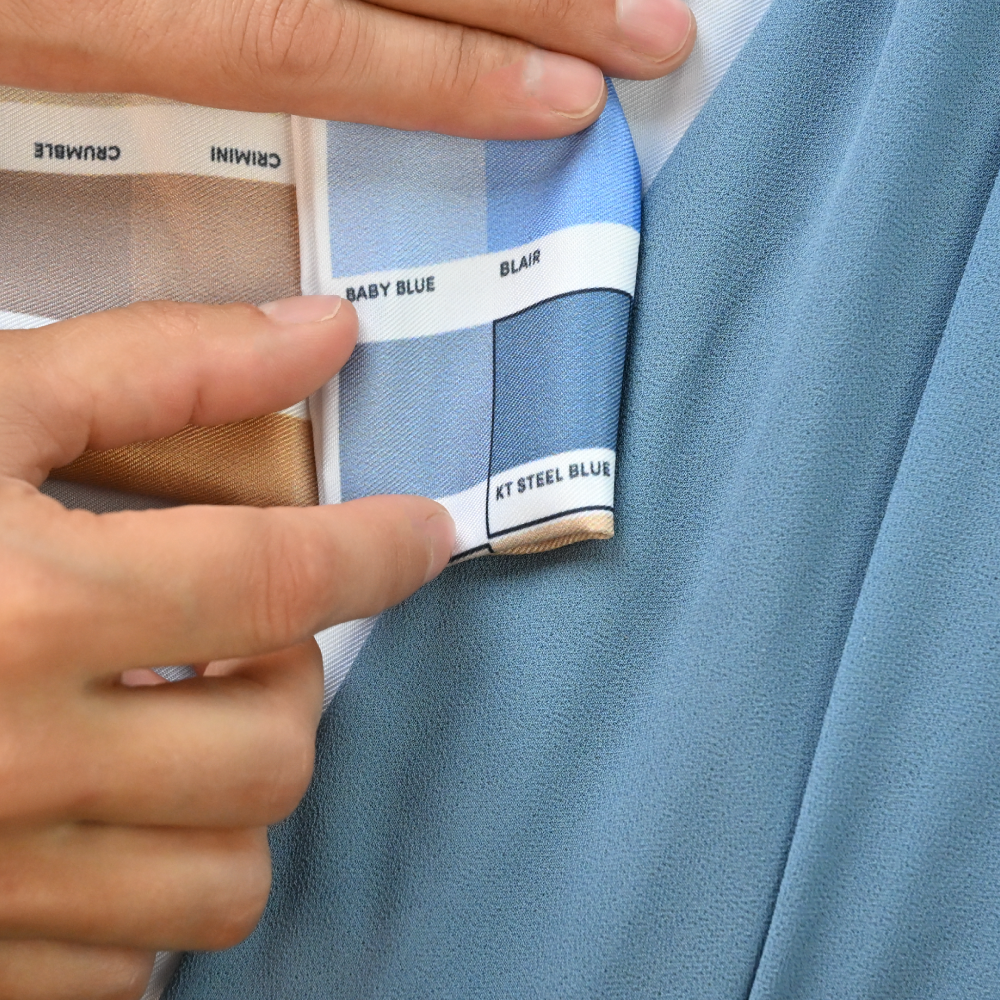 person holding a blue color swatch up to a matching blue bridesmaid's dress