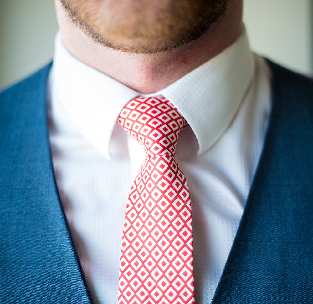 Geometric red and white colored necktie knot worn with navy blue vest
