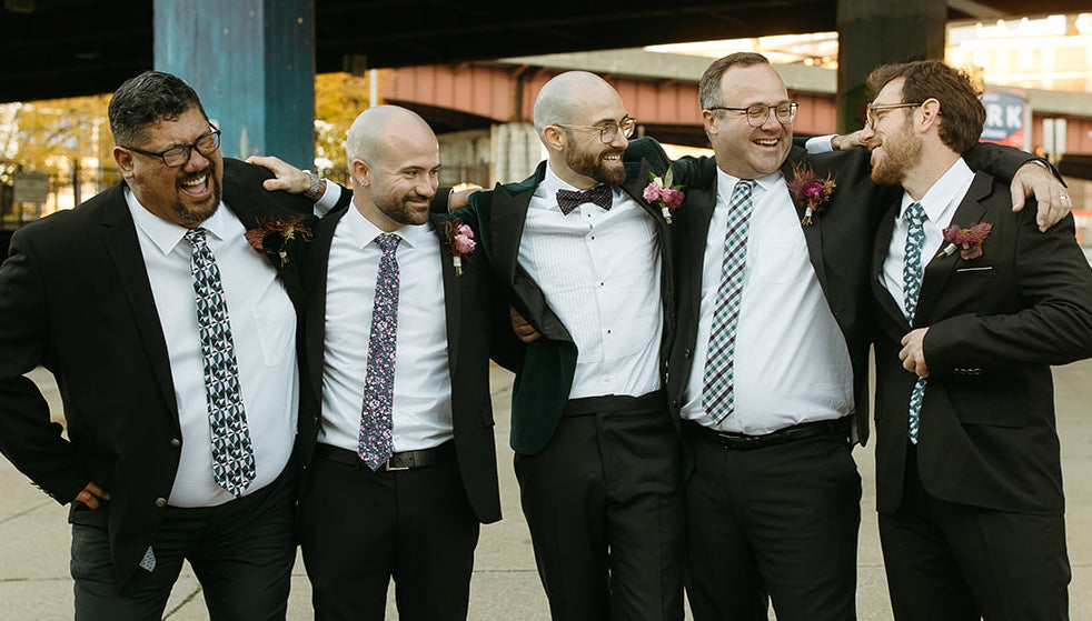 Five men hugging in dark suits with different patterned ties and bow tie