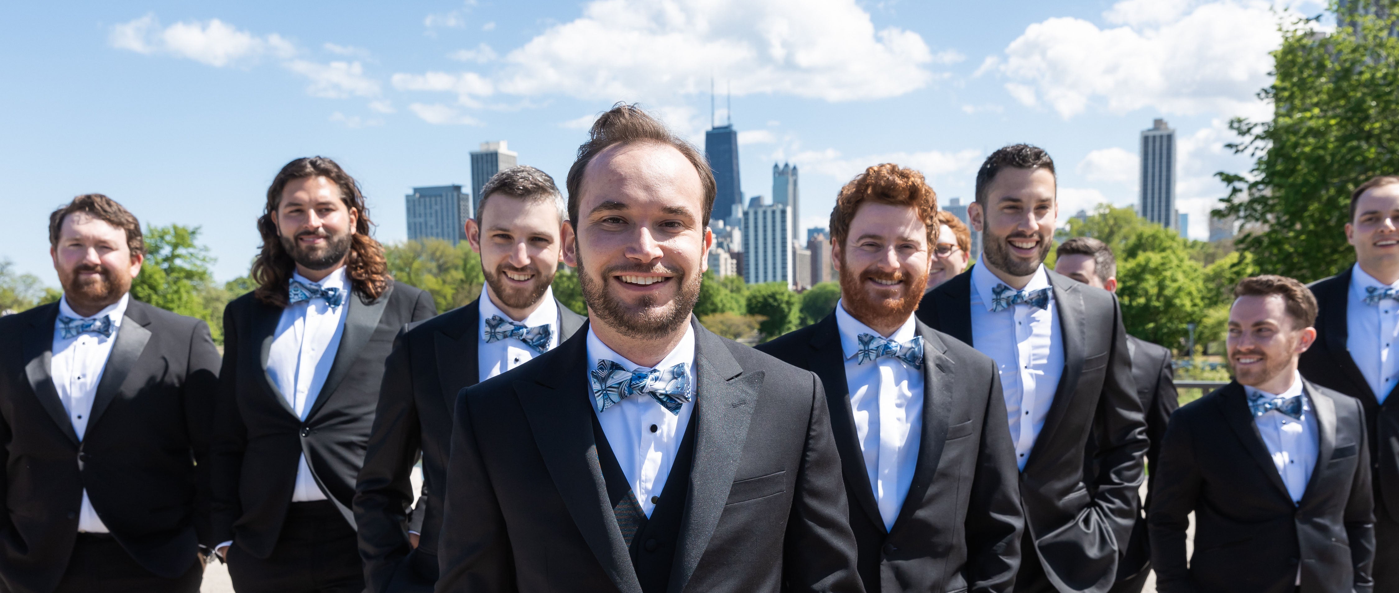 Groom and groomsmen wearing custom bow ties and black suits in front of a city skyline