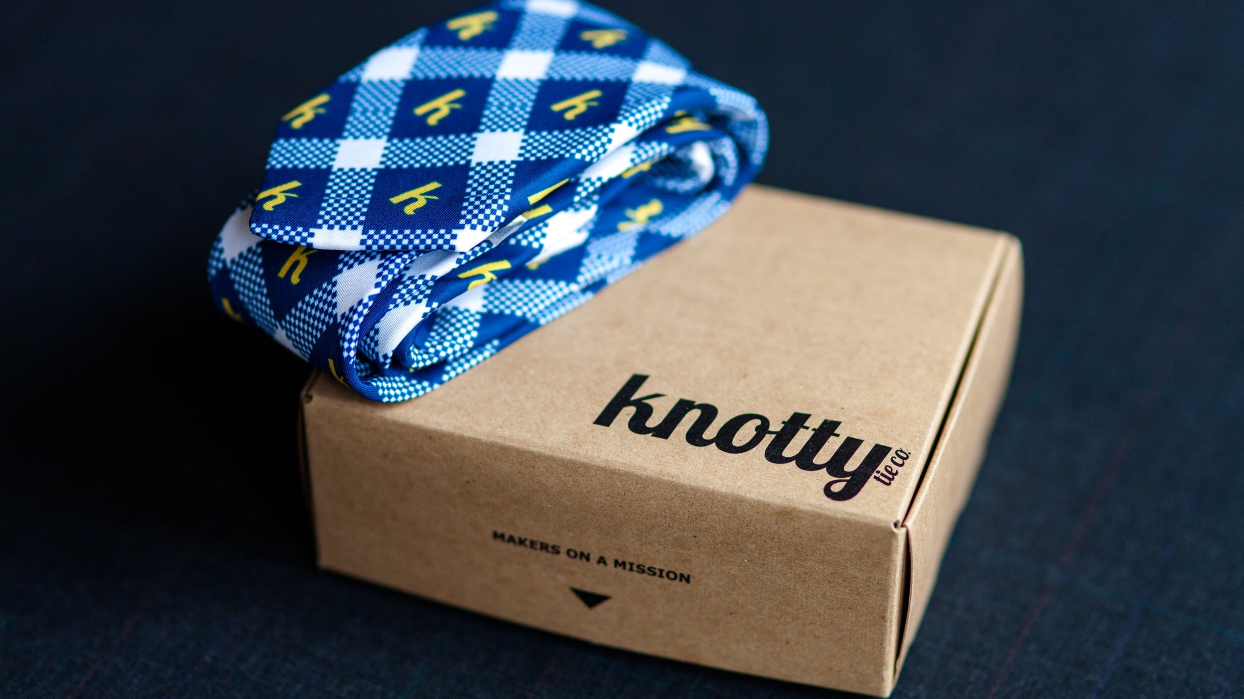 Navy and white plaid rolled necktie with custom logo featured set on top of kraft box packaging