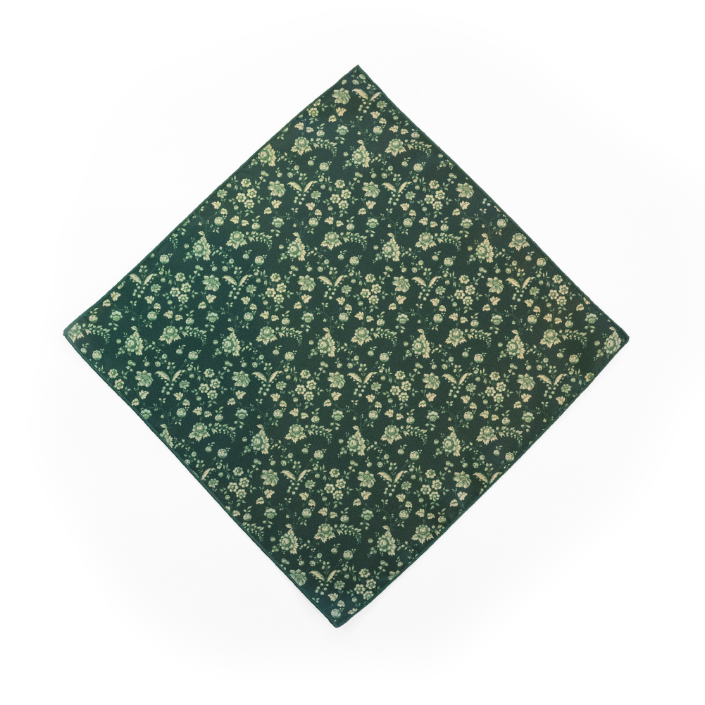 A pocket square with a dense floral print in sage green and cream on a dark forest green background.