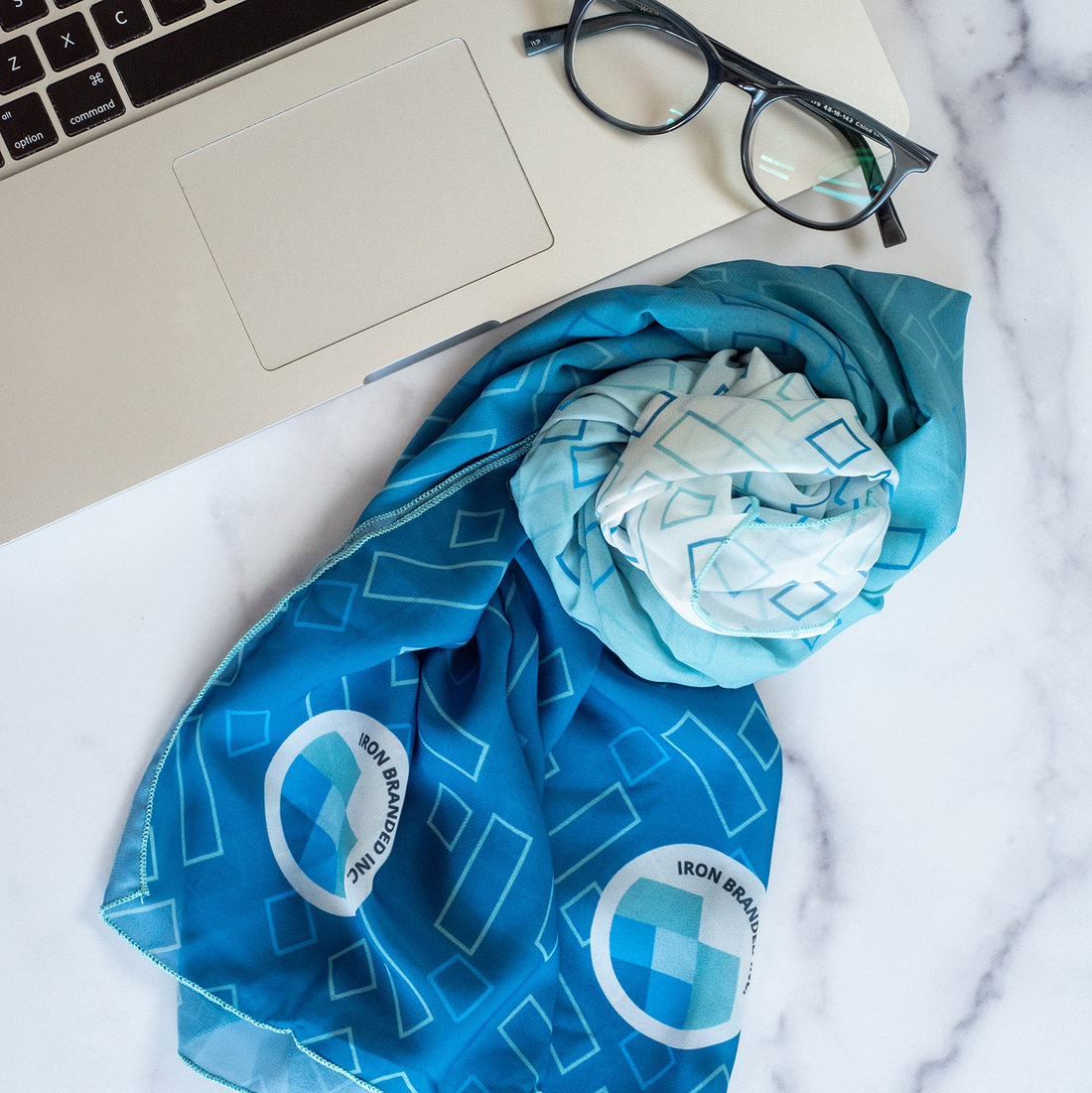 Blue patterned scarf with logos over a laptop on a marble surface