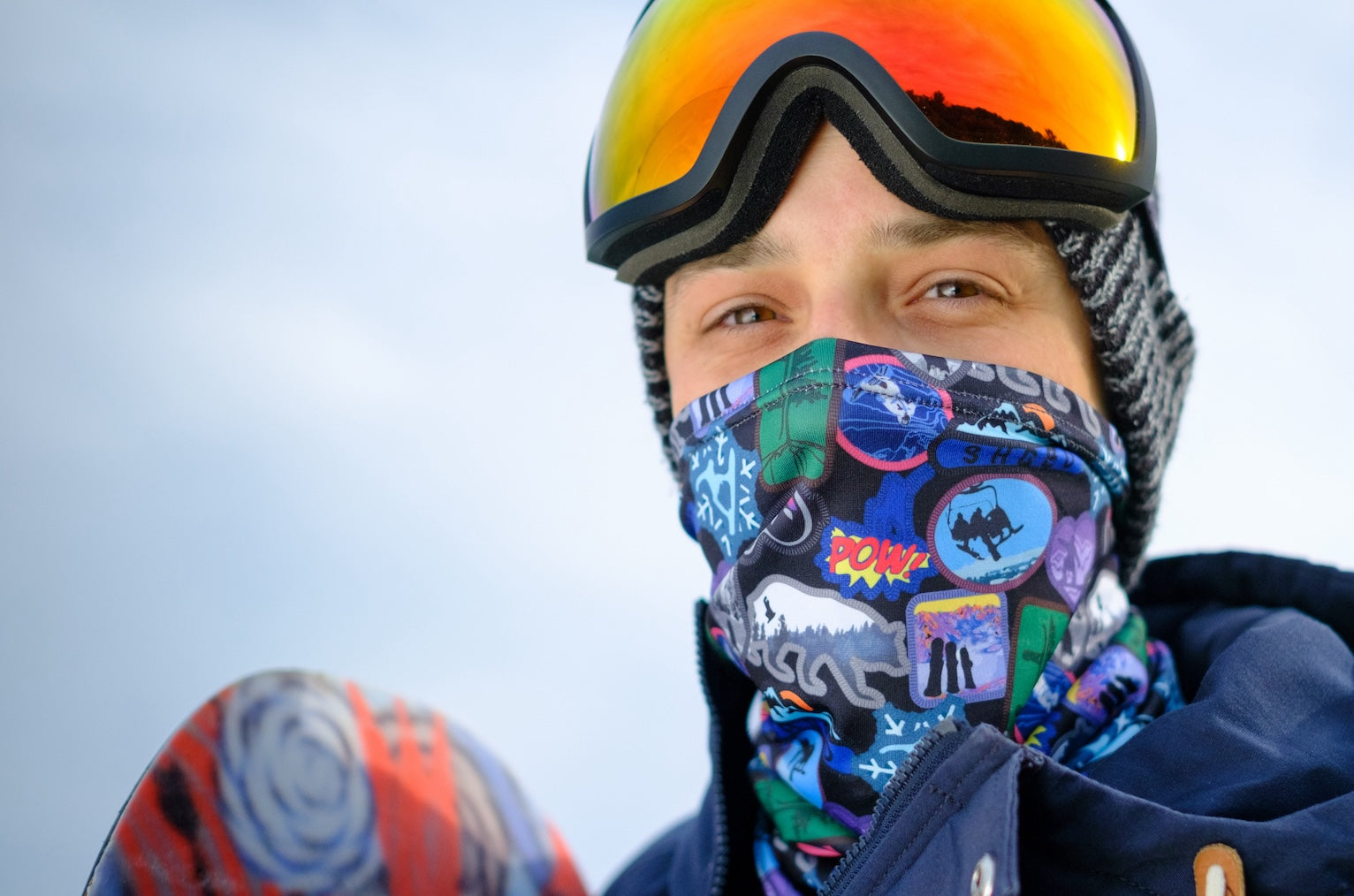 Man wearing custom neck gaiter and goggles while holding snowboard