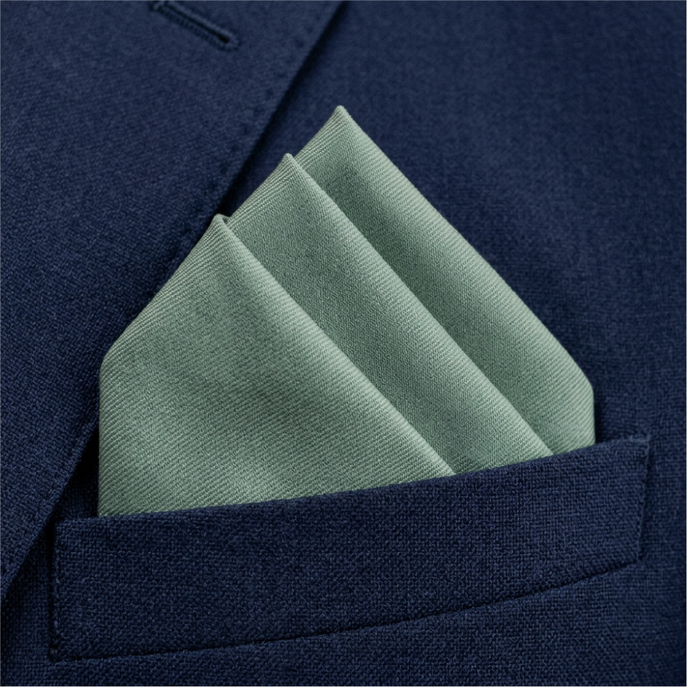 A folded sage green pocket square tucked into the breast pocket of a textured navy blue suit jacket.