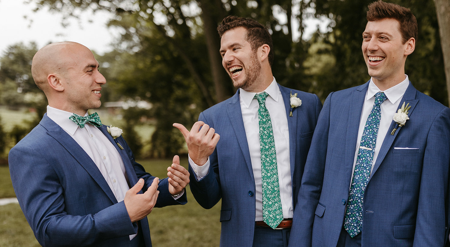 Three men wearing navy suits wearing floral bow tie and neckties
