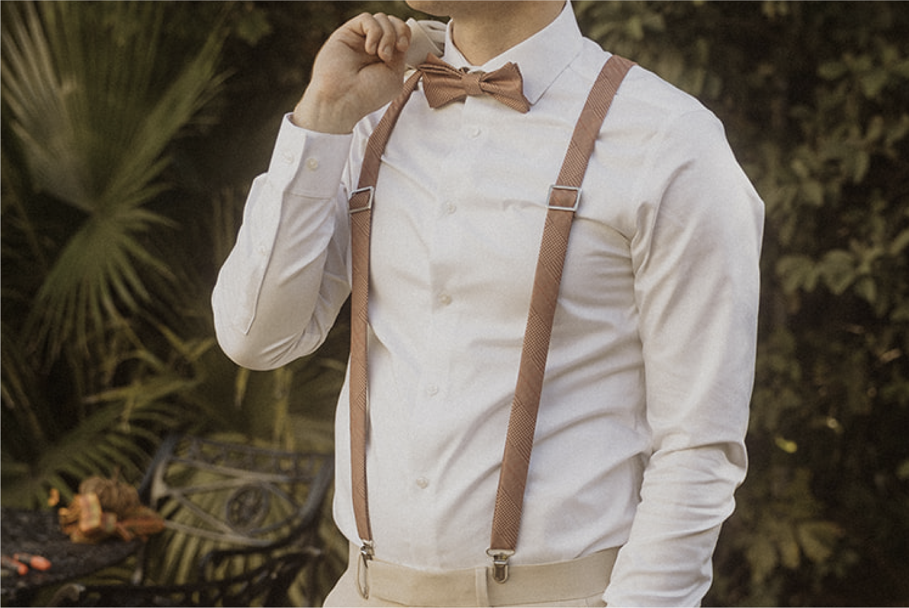 Person wearing a white shirt, brown bow tie, and suspenders against a natural background.
