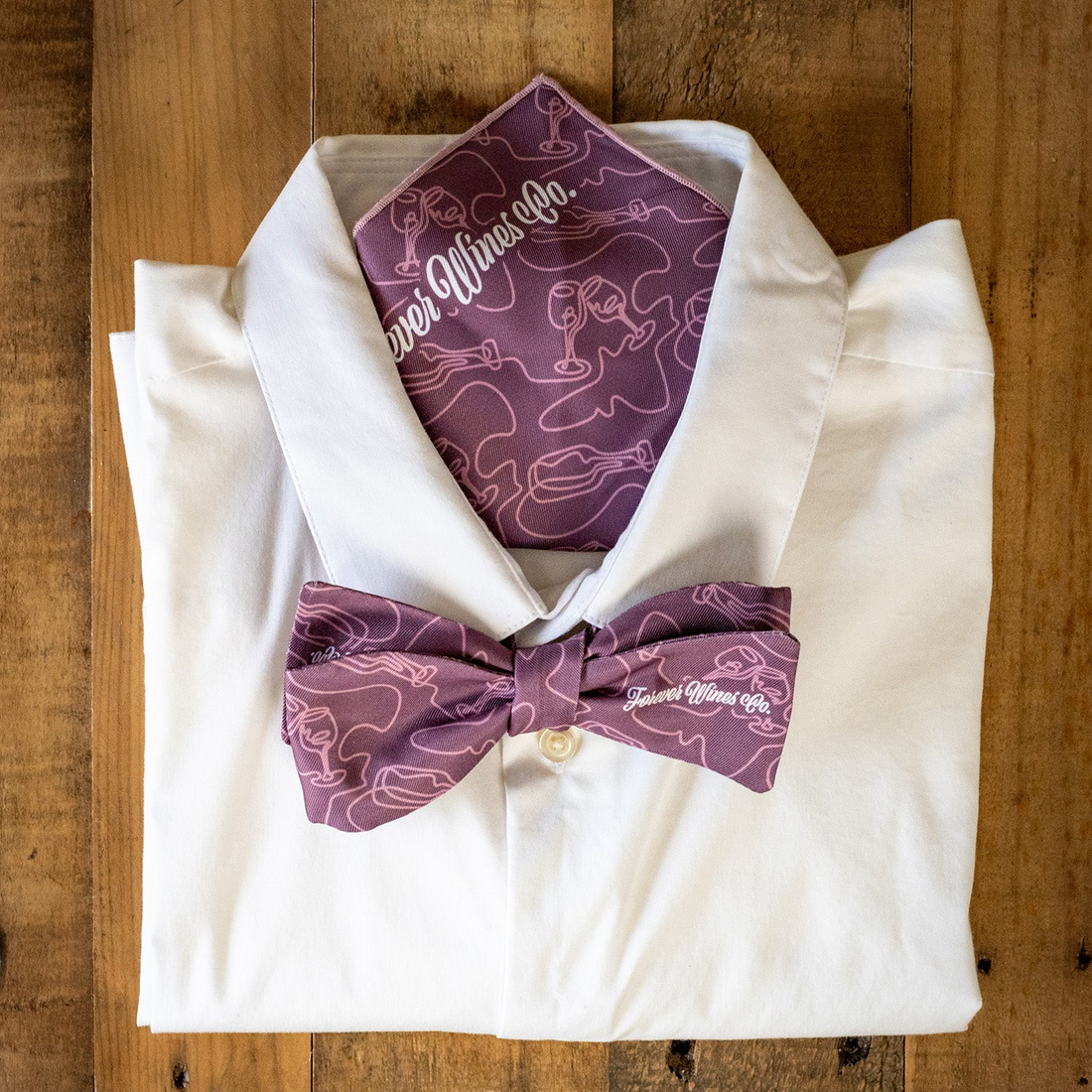 White shirt with purple bow tie and pocket square on a wooden surface