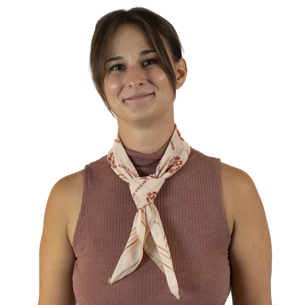 A woman wearing a dusty rose top and a tied cream square scarf around her neck.