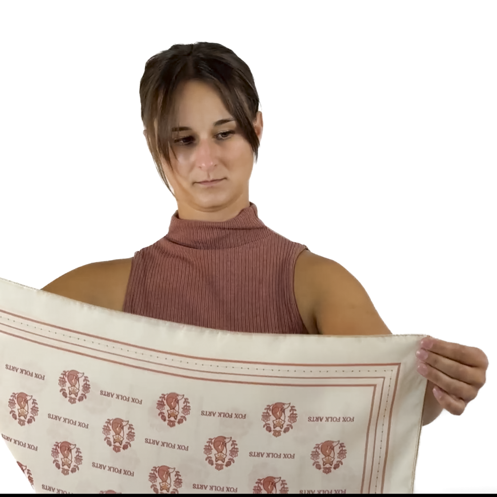 A woman holding up a cream square scarf folding it into a triangle
