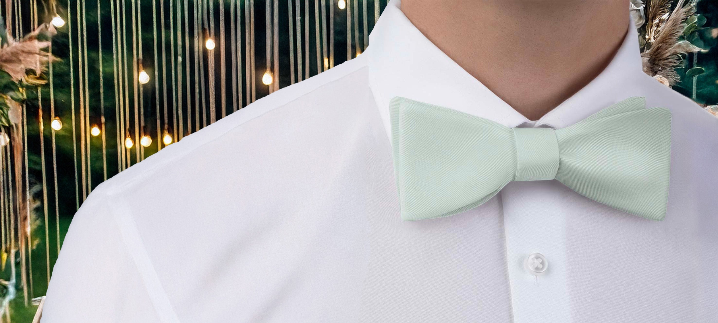 Person wearing a light green bow tie matched to Azazie dresses with a blurred decorative background