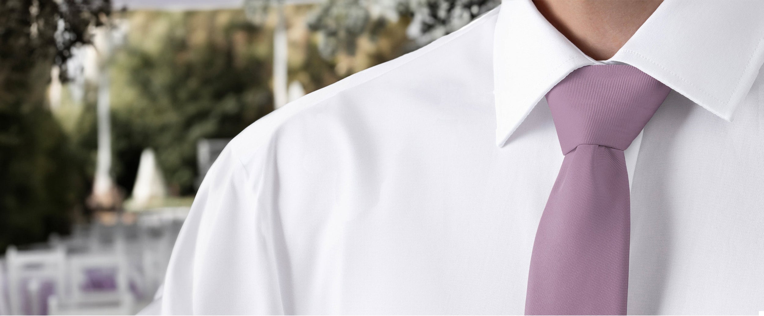 Close-up of a person wearing a white shirt and a purple tie with a blurred outdoor background.