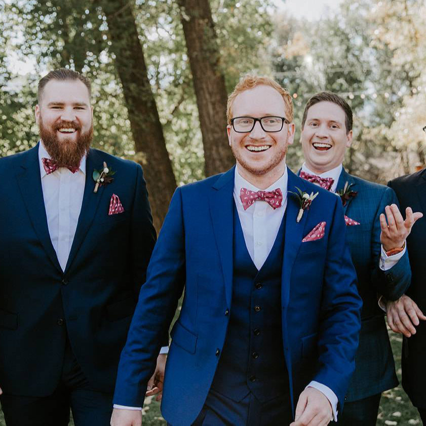 groom and groomsmen wearing blue suits and red bow ties and pocket squares