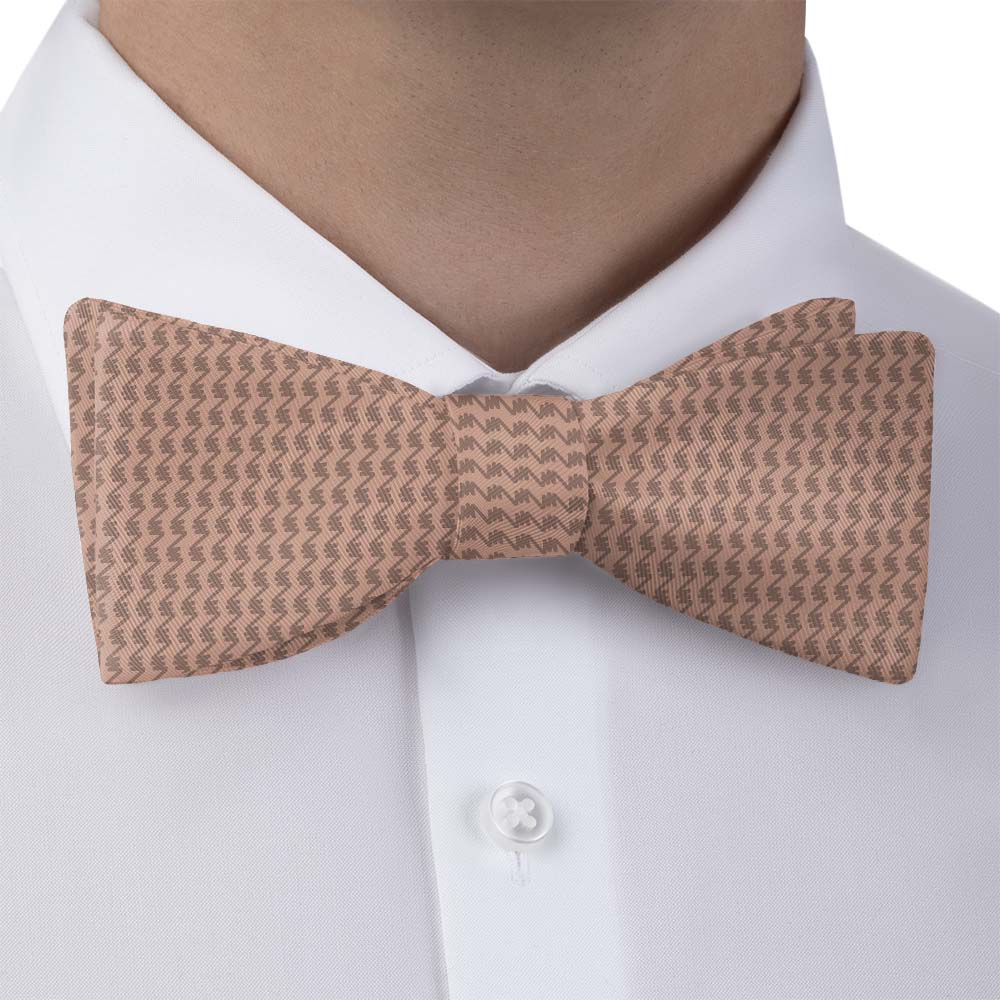 Brown patterned bow tie worn by a person on a white shirt.