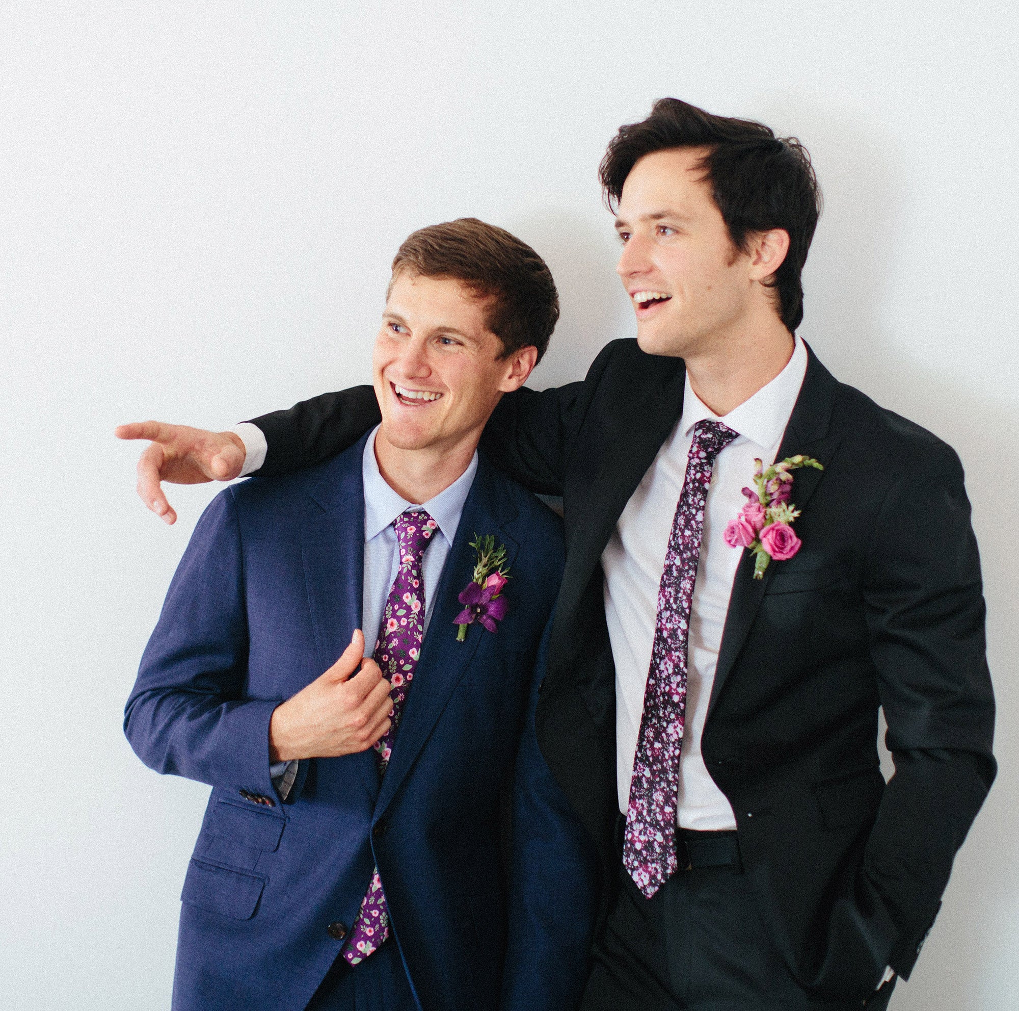 Two guys in suits and floral ties smiling and pointing