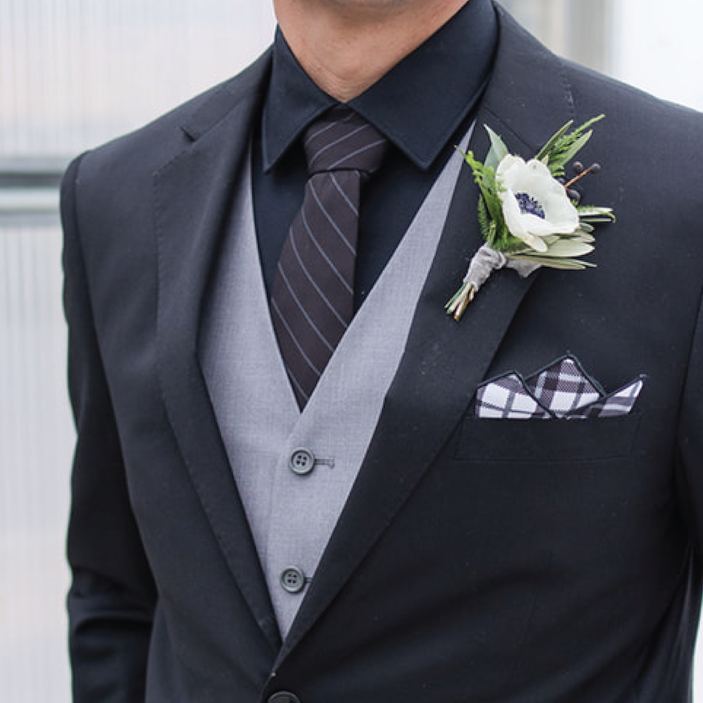 Man wearing a formal black suit with a white flower boutonniere and striped tie.