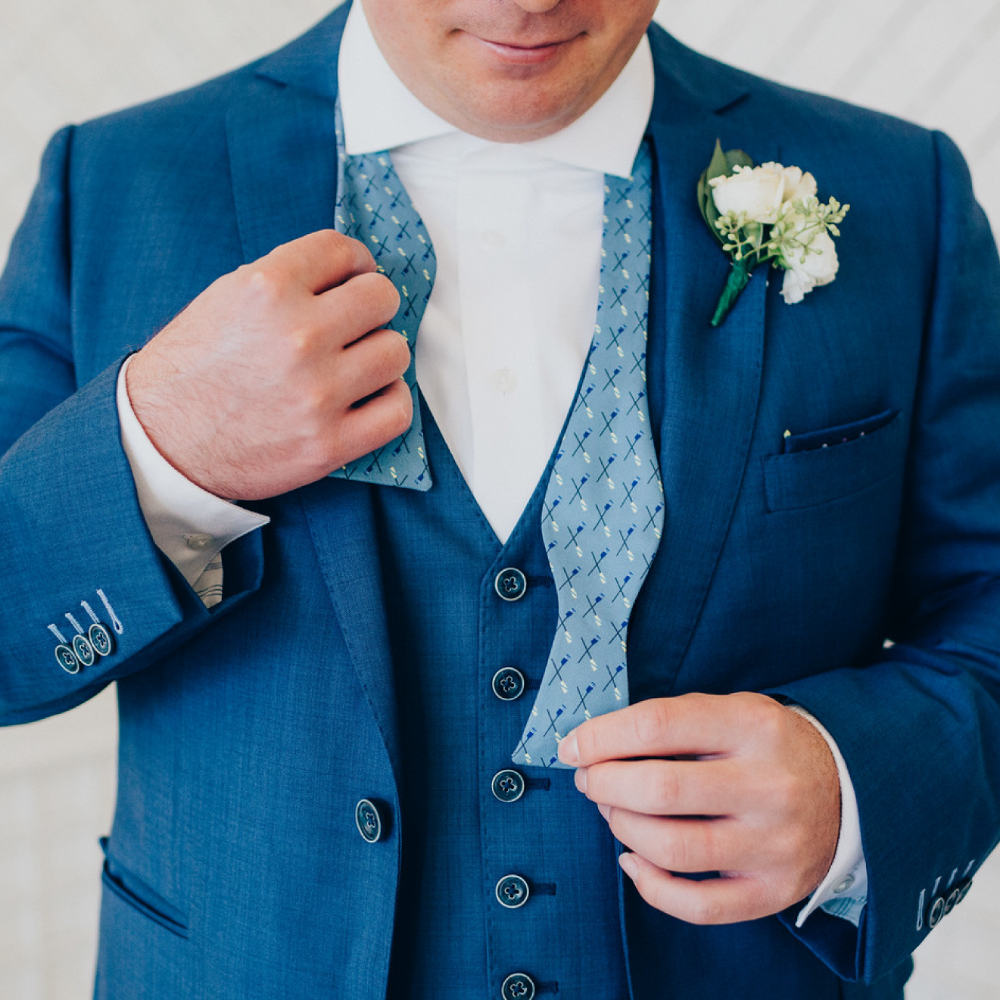 Man wearing a blue suit with a white shirt and floral boutonniere, adjusting his vest.