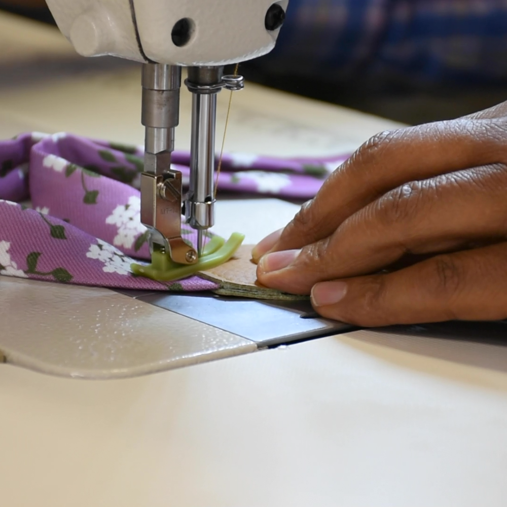 Person sewing suspenders with a floral pattern on a sewing machine.