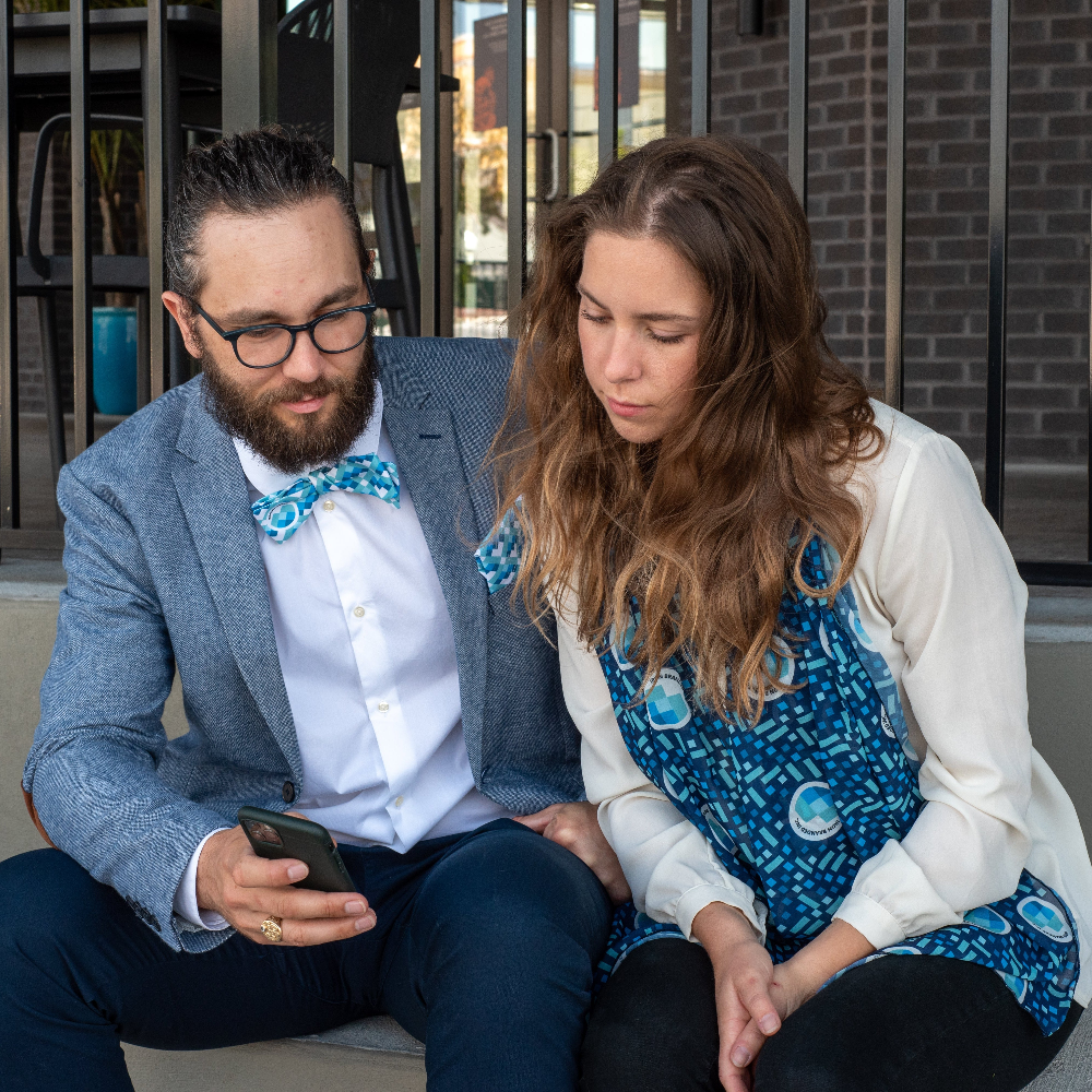Man wearing custom bow tie and woman wearing scarf sitting together.