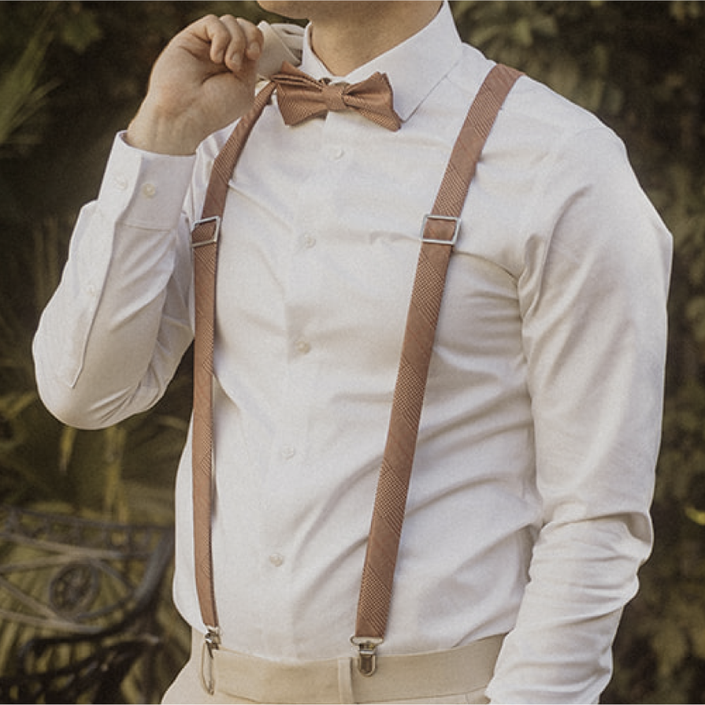 Person wearing a white shirt with brown suspenders and bow tie against a blurred natural background