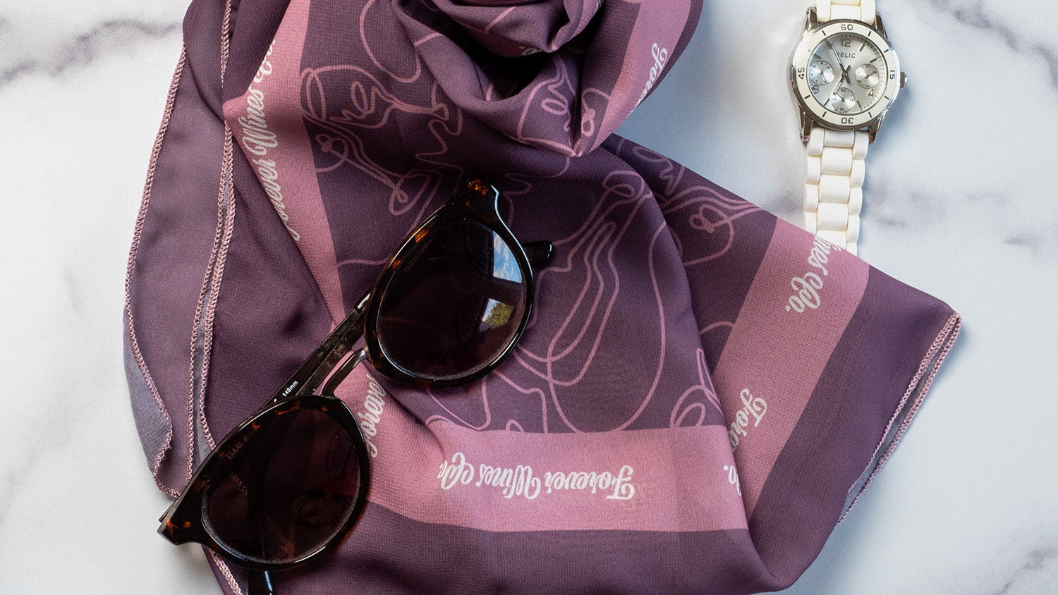 Purple scarf with white text, sunglasses, and watch on a marble surface