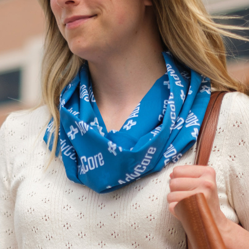 Woman wearing a blue scarf with white text, holding a brown bag.