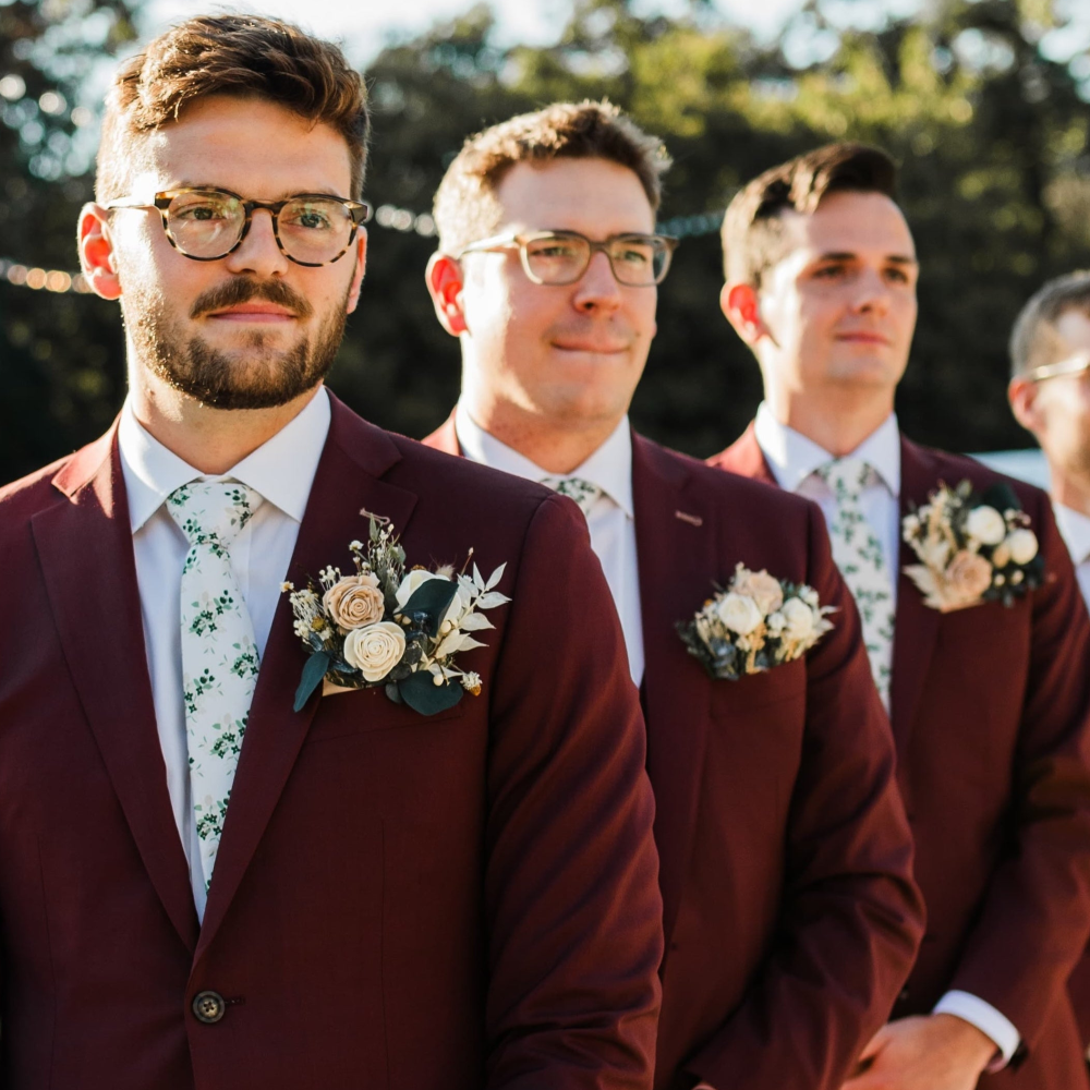 Men in burgundy suits with floral custom tie standing outdoors.