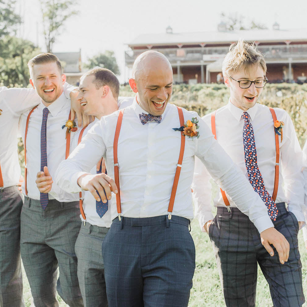 Group of men in formal attire with suspenders and ties outdoors.