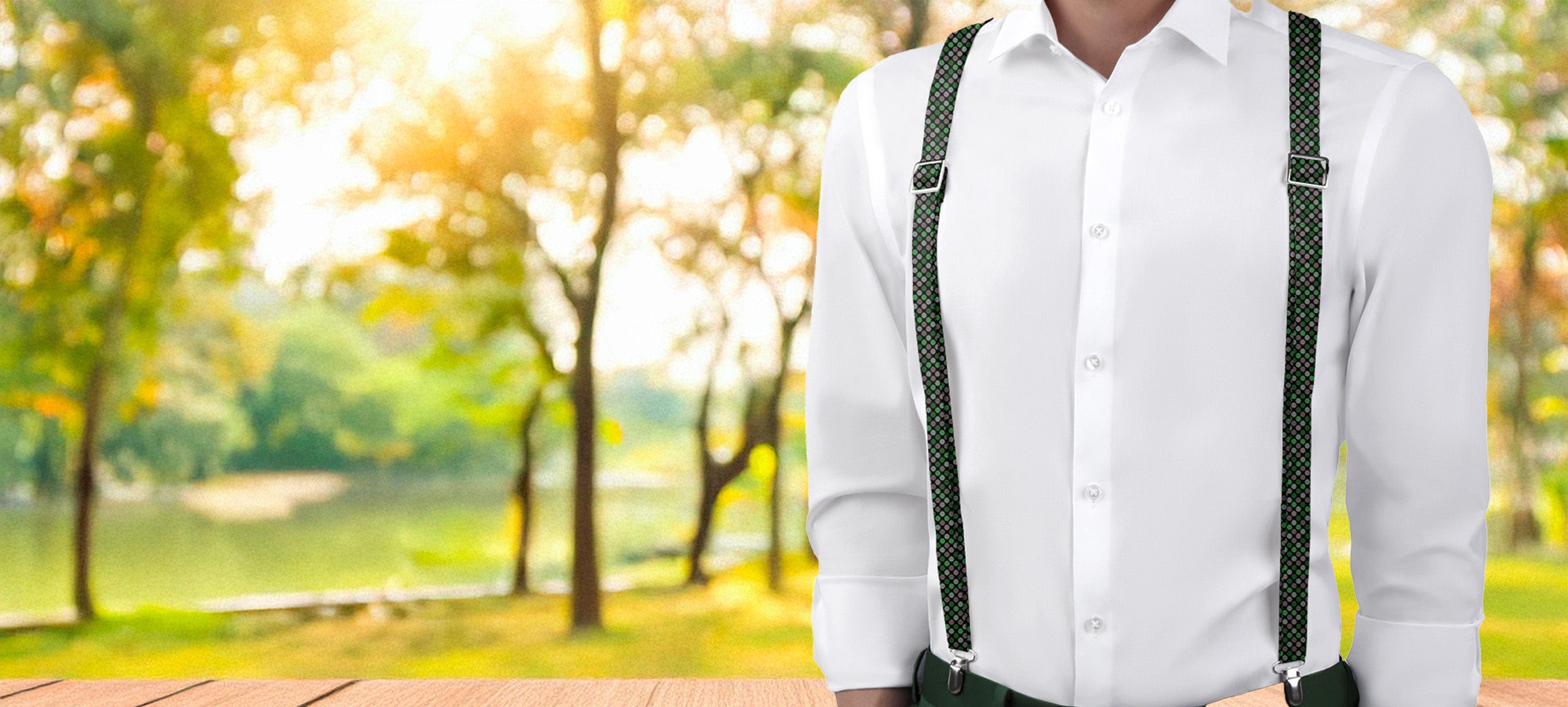 Person wearing dotted suspenders standing in a park with trees and sunlight.