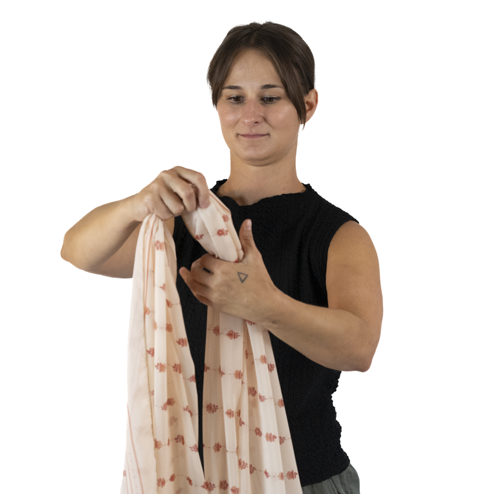 A woman holding a cream colored rectangle scarf and gathering the fabric