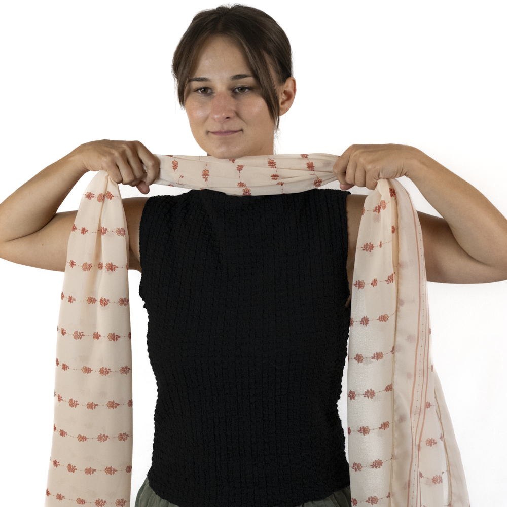 A woman holds up the gathered fabric of a rectangle scarf up to the front of her neck