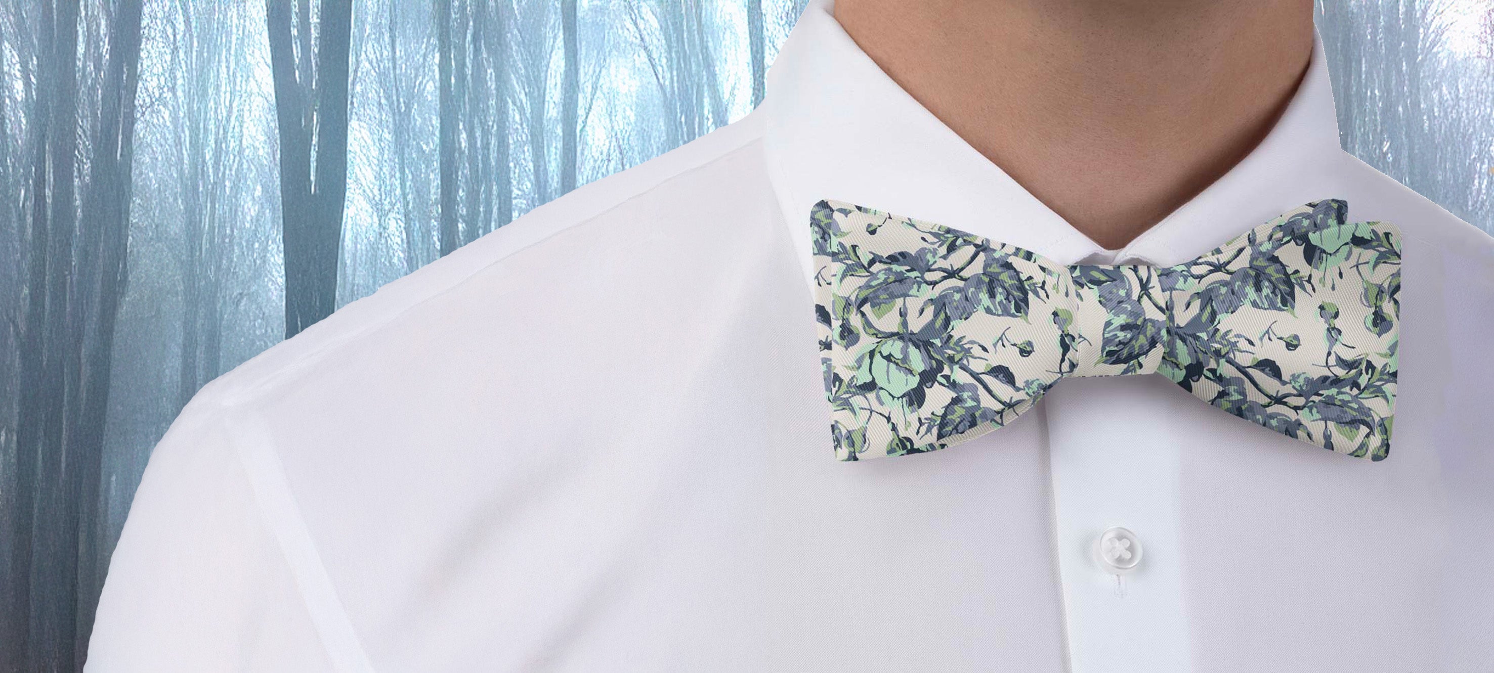 Person wearing a white shirt with a floral bow tie against a blurred forest background