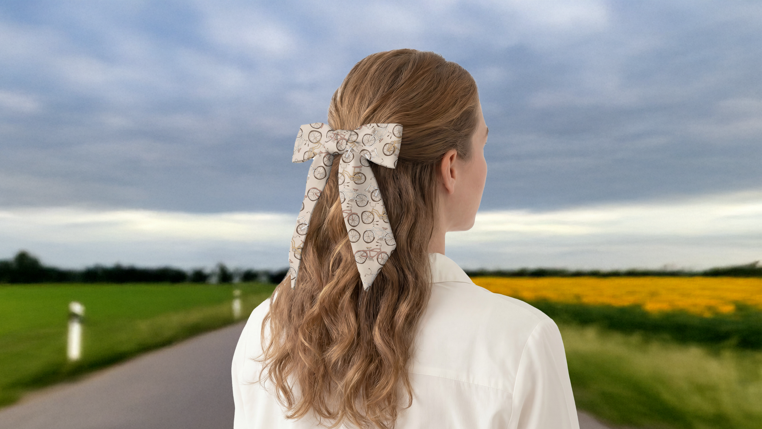 Person with a decorative hair scarf standing on a road with a field and sky in the background